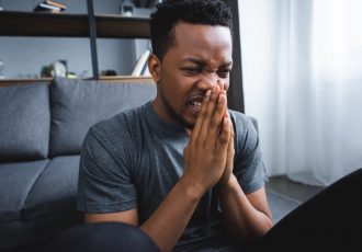stressed african american man with hands together suffering from panic attack at home